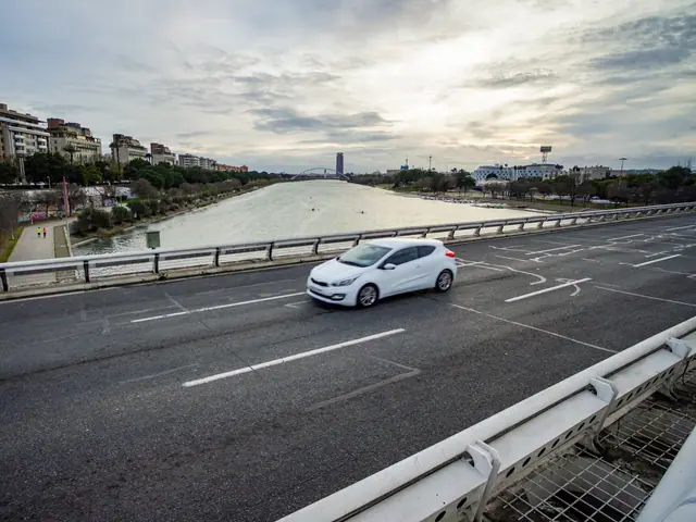 Carro branco passando numa ponte, com o rio e a cidade ao fundo