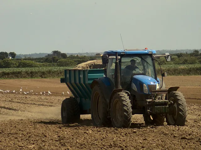 Trator azul puxando uma carreta num campo arado